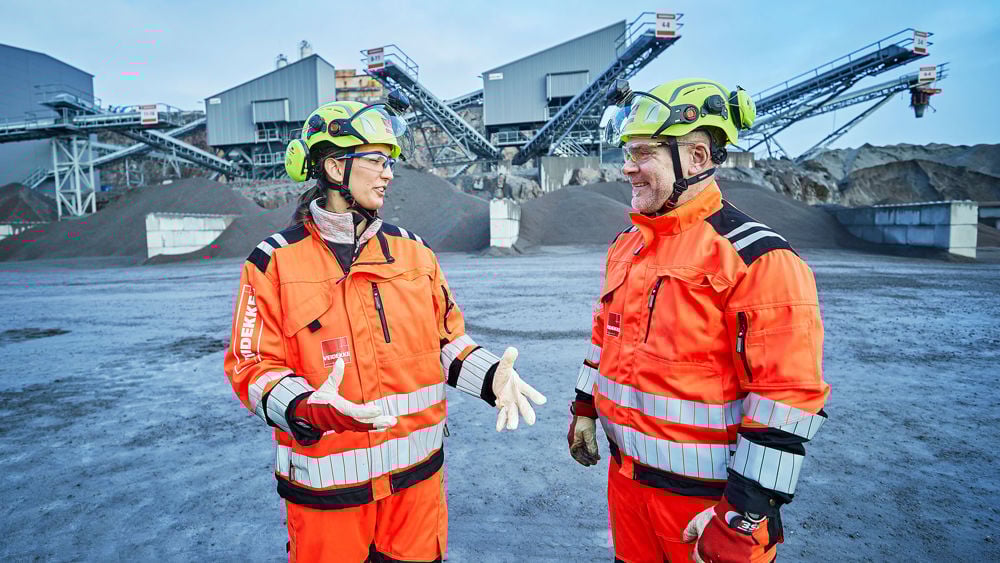 Två människor i bygghjälm och varselkläder diskuterar.