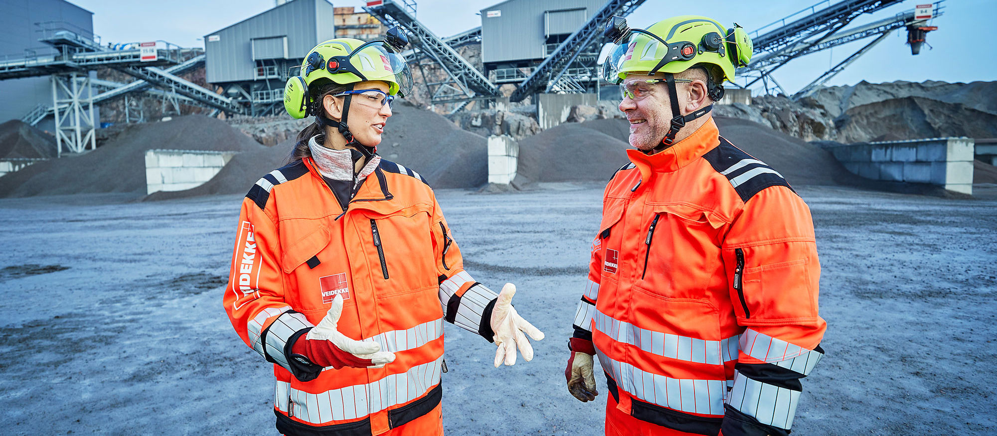 Två människor i bygghjälm och varselkläder diskuterar.