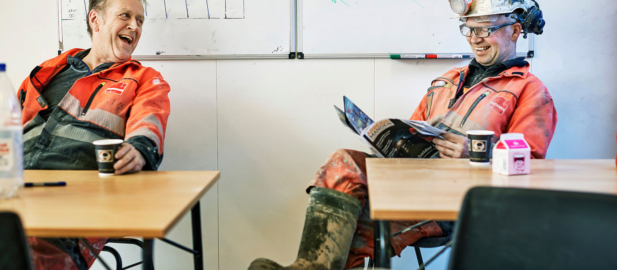 Två glada män sitter och pratar i en matsal på en arbetsplats.