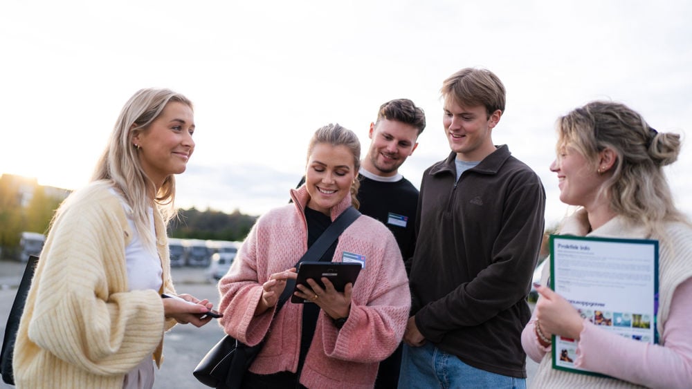 Fem personer diskuterar kring någon som visas på en ipad.