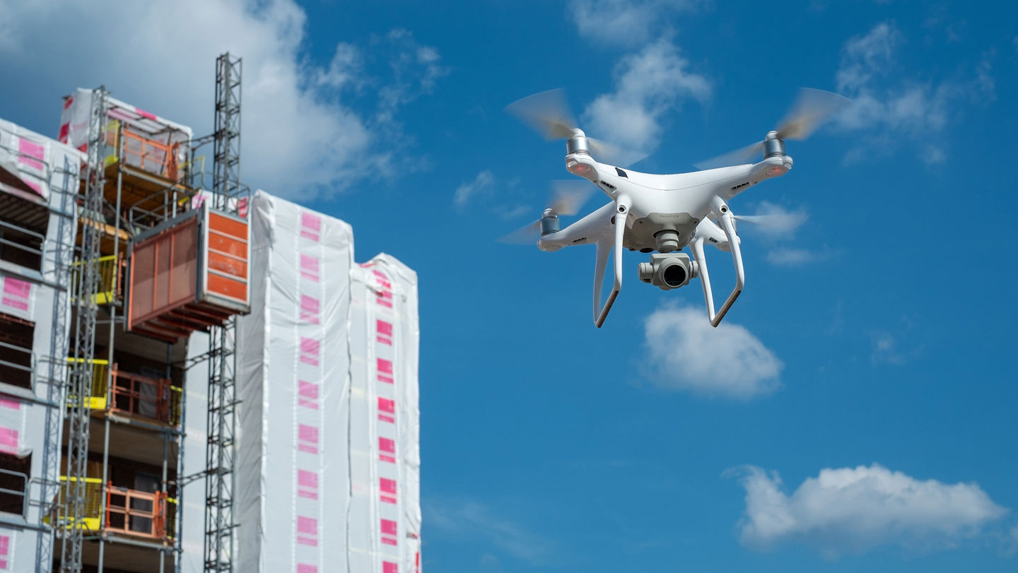 En drönare som flyger mot en blå himmel med ett byggprojekt i bakgrunden