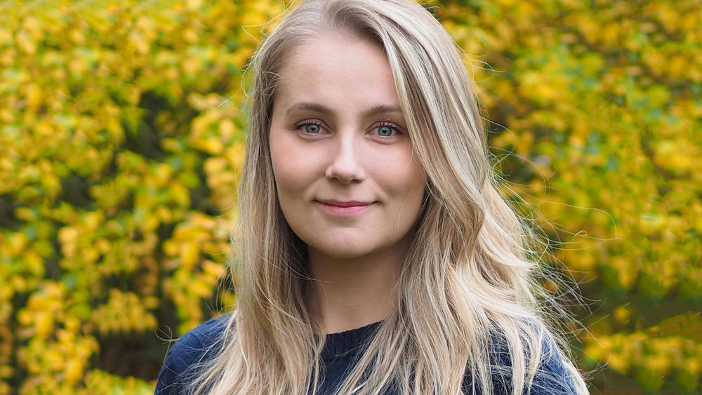 Josefine Olsson, blond kvinna framför gulgrönt buskage