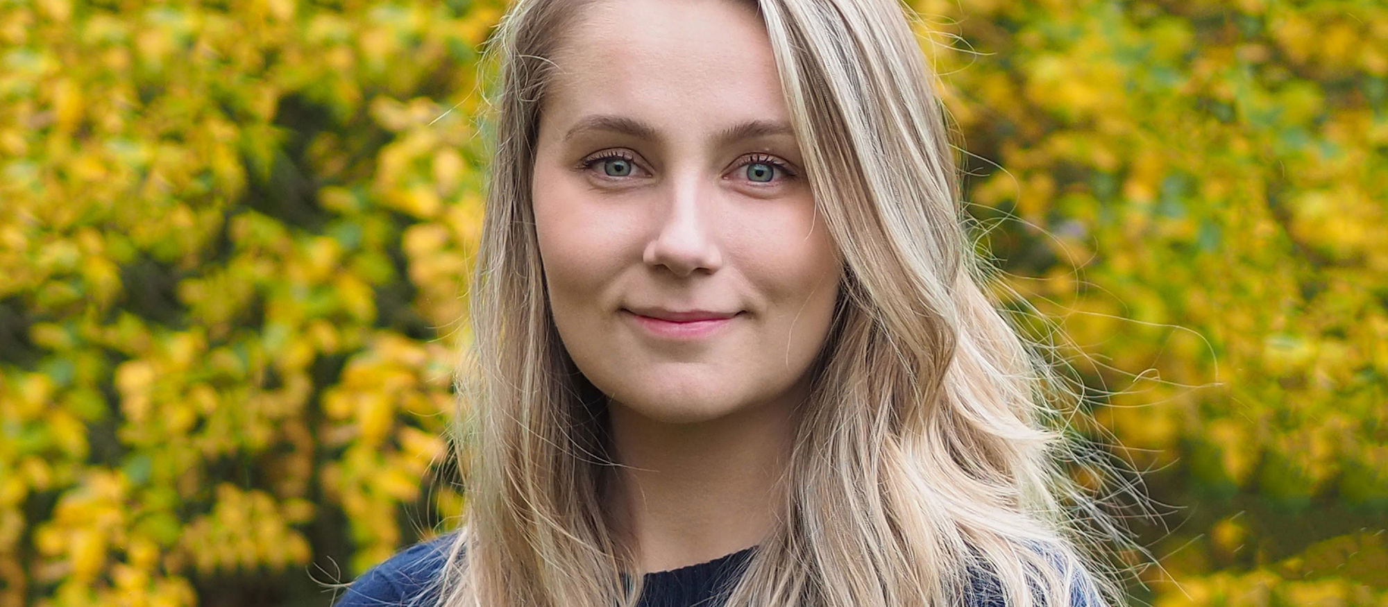 Josefine Olsson, blond kvinna framför gulgrönt buskage