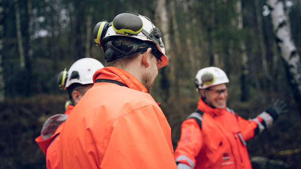 Tre byggarbetare framför en skog