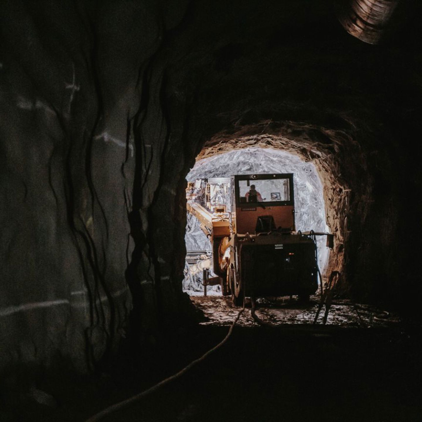 Mörk bergtunnel med anläggningsmaskin i ljuset i mynningen