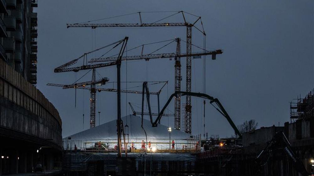 Byggkranar mot natthimmel med ett stort upplöst tält på marken där arbete pågår
