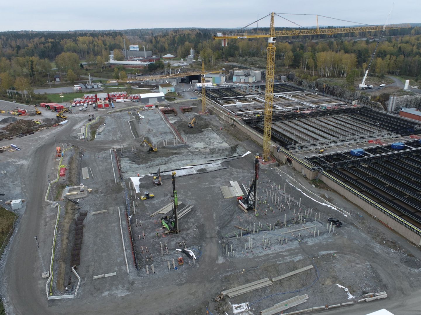 Drönarbild över pågående arbete vid Himmerfjärdsverket. Håltagning, gula byggkranar och stora ytor frilagd mark. Röda byggbodar i bakgrund och bassänger i högerkant. 