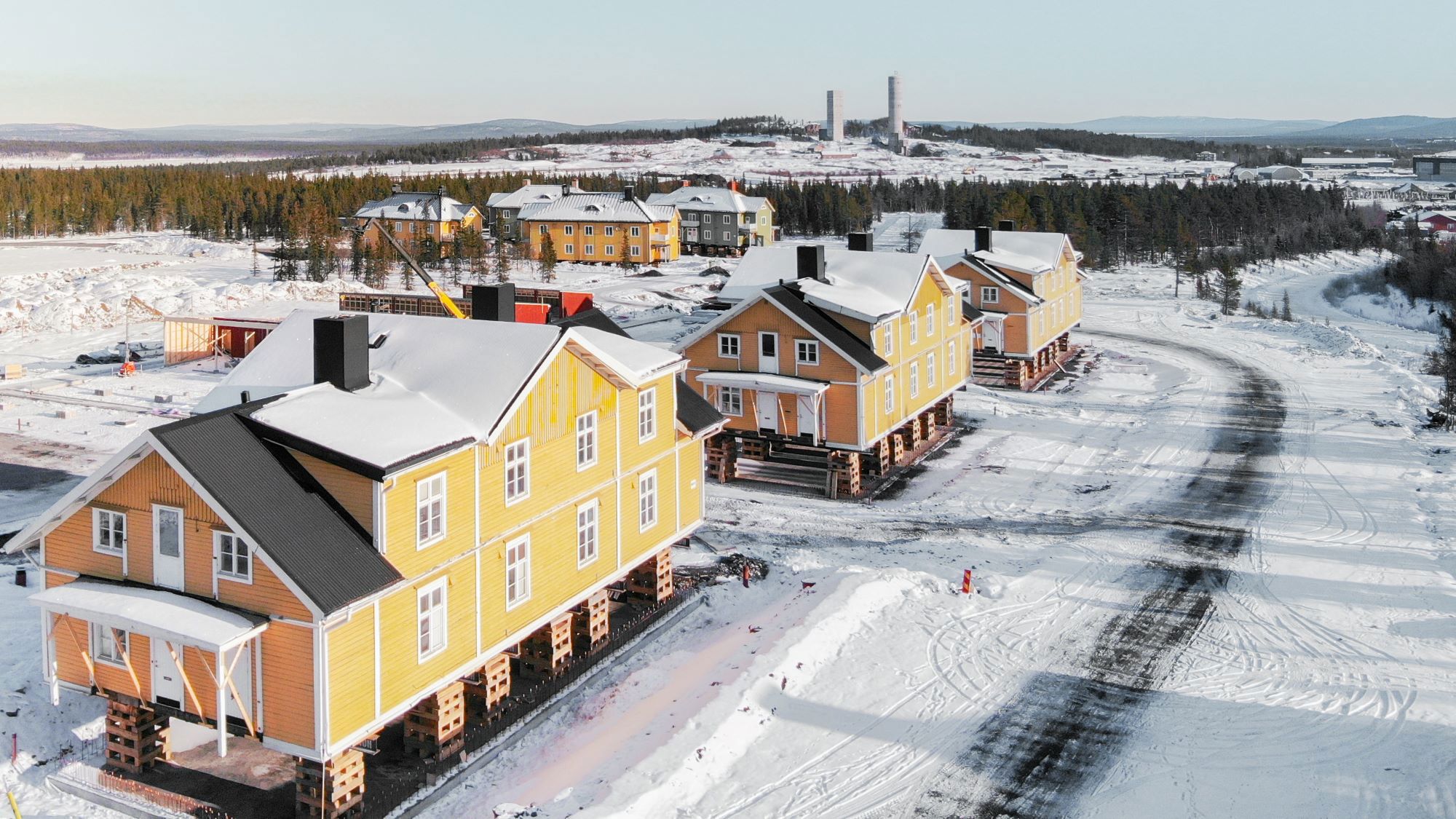 Vi flyttar “Gula raden” i Kiruna. Tre stora gula trähus har lyfts upp på pallar ovanför marken i snöig omgivning. 