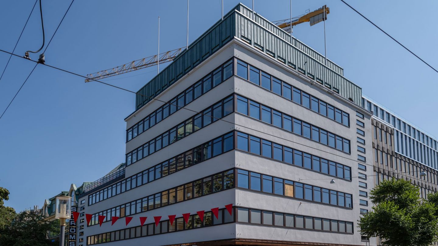 Ljus flervåningsbyggnad i funkisstil med gul byggkran svävande ovanför