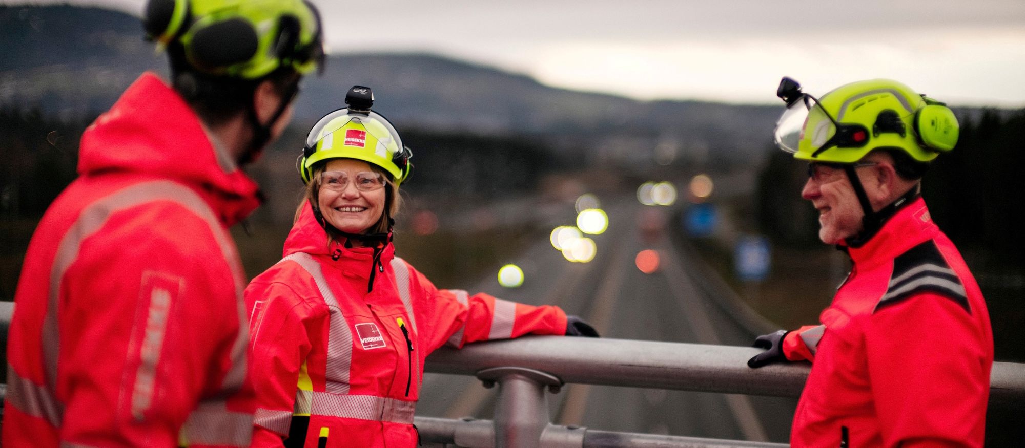 Tre människor i varselkläder samtalar på en bro